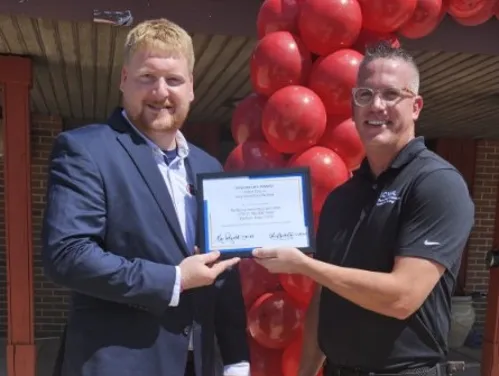 two men standing in front of a building holding a certificate